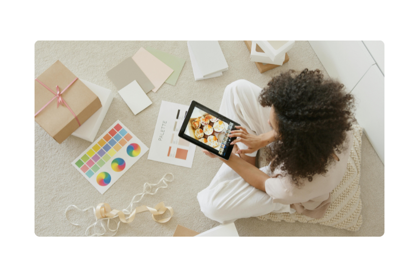 Een vrouw die onderzoekt hoe ze op Amazon kan verkopen, met behulp van een tablet terwijl ze wordt omringd door verpakkingen en ontwerpmaterialen.